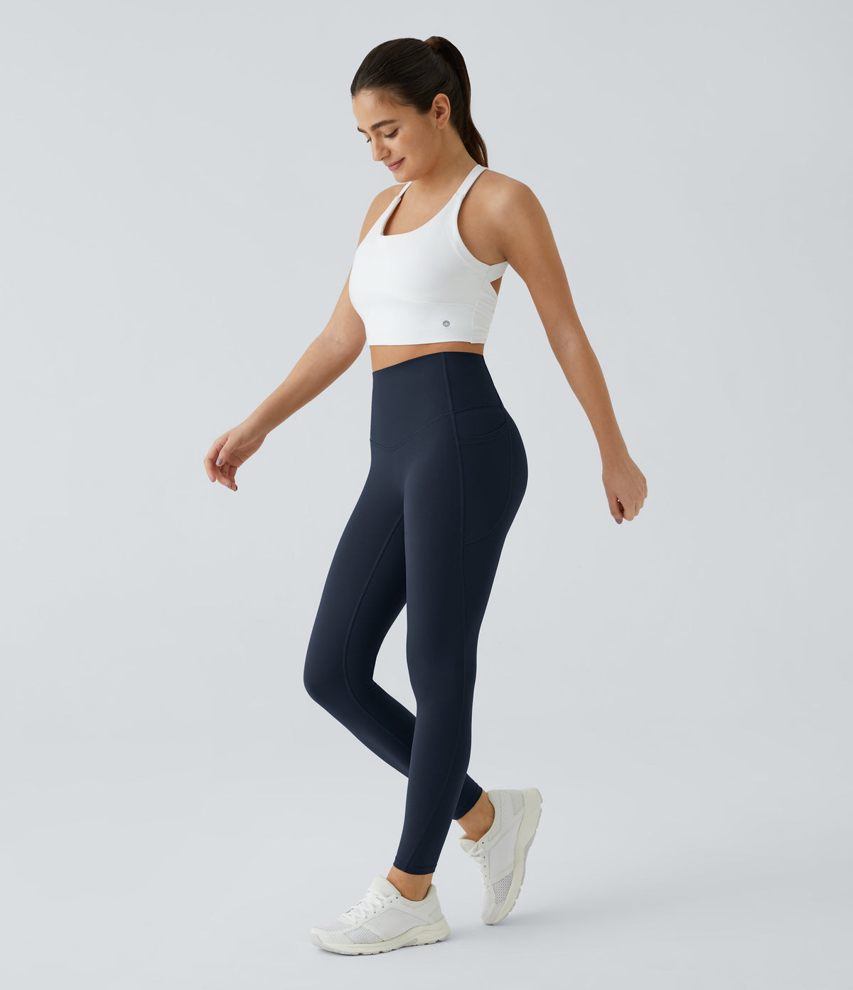 Model walking in Celeste L'Amour Carbon high-waisted 7/8 leggings with a white sports bra